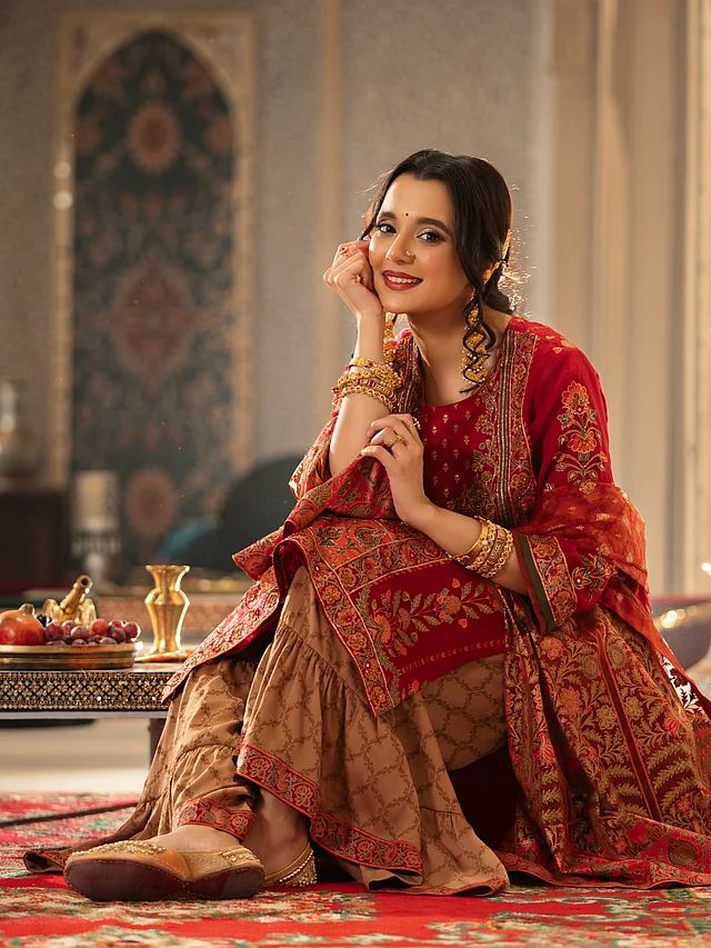 সাবিলা নূর পরেছেন লাল সারারা সালোয়ার-কামিজ, যার রাউন্ড নেকলাইন ও থ্রি-কোয়ার্টার স্লিভে ফুটে উঠেছে সূক্ষ্ম কারচুপি ও এমব্রয়ডারি করা ফ্লোরাল মোটিফ। সঙ্গে ম্যাচ করেছেন আর্দি টোনের ফারসি (সারারা) প্যান্ট এবং লাল ম্যাচিং ওড়না, যা পুরো থ্রি-পিস সেটকে সম্পূর্ণ করেছে। এই ধরনের আউটফিটের সঙ্গে সাধারণত পায়ে জুত্তি বেশি মানায়।