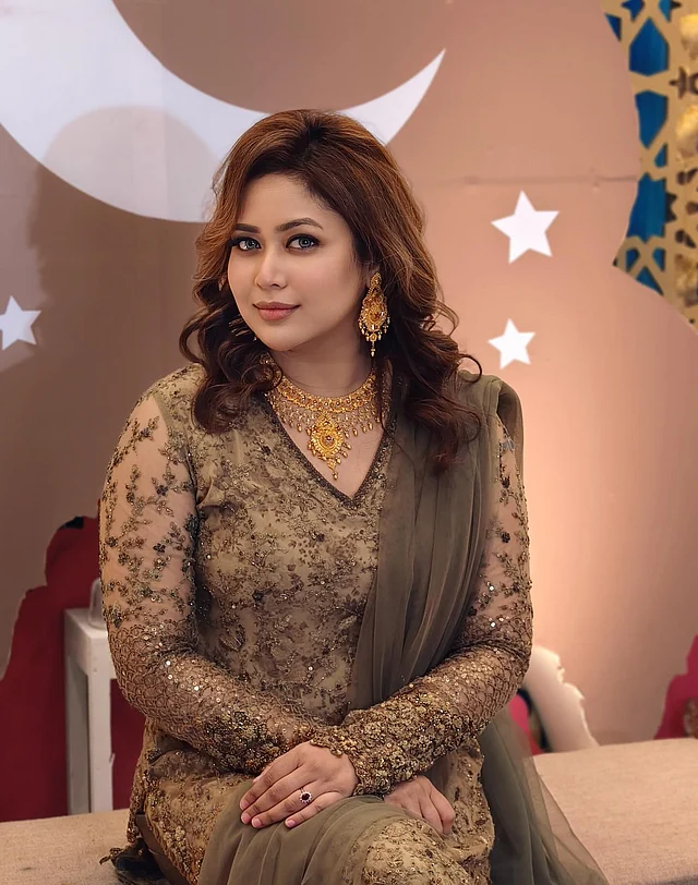 সুন্দরী অভিনেত্রী ভাবনার এই লুকে ধরা পরেছে এক রাজকীয় সৌন্দর্য। তিনি পরেছেন ডার্ক অলিভ - গোল্ড টোনের সালোয়ার কামিজ।শিয়ার ফেব্রিকের পুরো ড্রেস জুড়ে সূক্ষ্ম এমব্রয়ডারি ও সিকুইনের ফ্লোরাল কারুকাজ দেখা যাচ্ছে। এর সঙ্গে মিলিয়ে নিয়েছেন একই রঙের অলিভ টোনের সফট ওড়না। এই লুকের অন্যতম আকর্ষণ ভাবনার গয়না। গলায় পরেছেন গোল্ড নেকলেস,  কানে রয়েছে লম্বা দুল, হাতে একটি স্টোন সেট করা আংটি তাঁর সাজে যোগ করেছে আলাদা মাত্রা। মেকআপেও রাখা হয়েছে সফট গ্ল্যাম টাচ, যা পুরো লুককে আরও পূর্ণতা দিয়েছে। ঈদে এমন সাজ পারফেক্ট