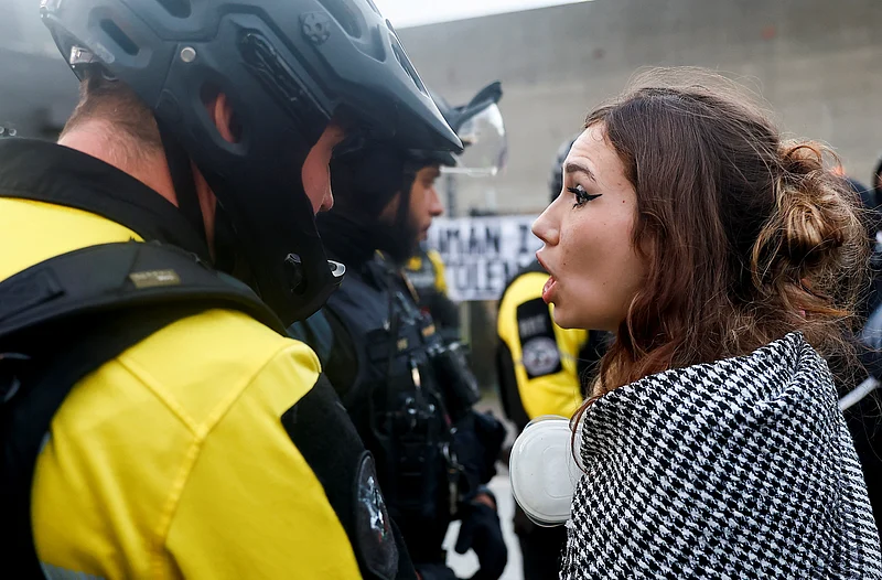 মার্কিন প্রেসিডেন্ট ডোনাল্ড ট্রাম্পের প্রশাসনিক নীতির বিরুদ্ধে আয়োজিত বিক্ষোভ কর্মসূচিতে অংশ নেওয়া একজনকে আইনশৃঙ্খলা রক্ষাকারী বাহিনীর মুখোমুখি দাঁড়িয়ে প্রতিবাদ জানাতে দেখা যাচ্ছে। ওরেগন, ২৮ মার্চ