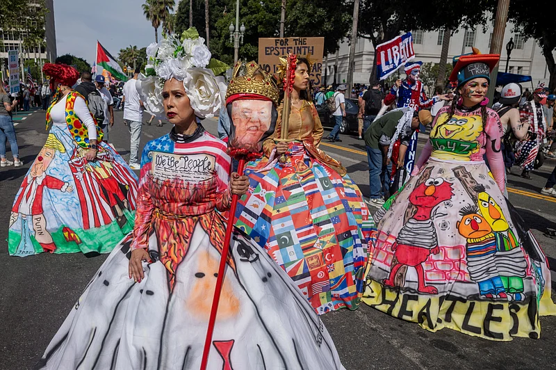 ডোনাল্ড ট্রাম্পের মাথায় মুকুট পরানো ছবি নিয়ে নানা রঙের পোশাক পরে ‘নো কিংস’ বিক্ষোভে অংশ নিয়েছেন মার্কিন নাগরিকেরা। লস অ্যাঞ্জেলেস, ২৮ মার্চ