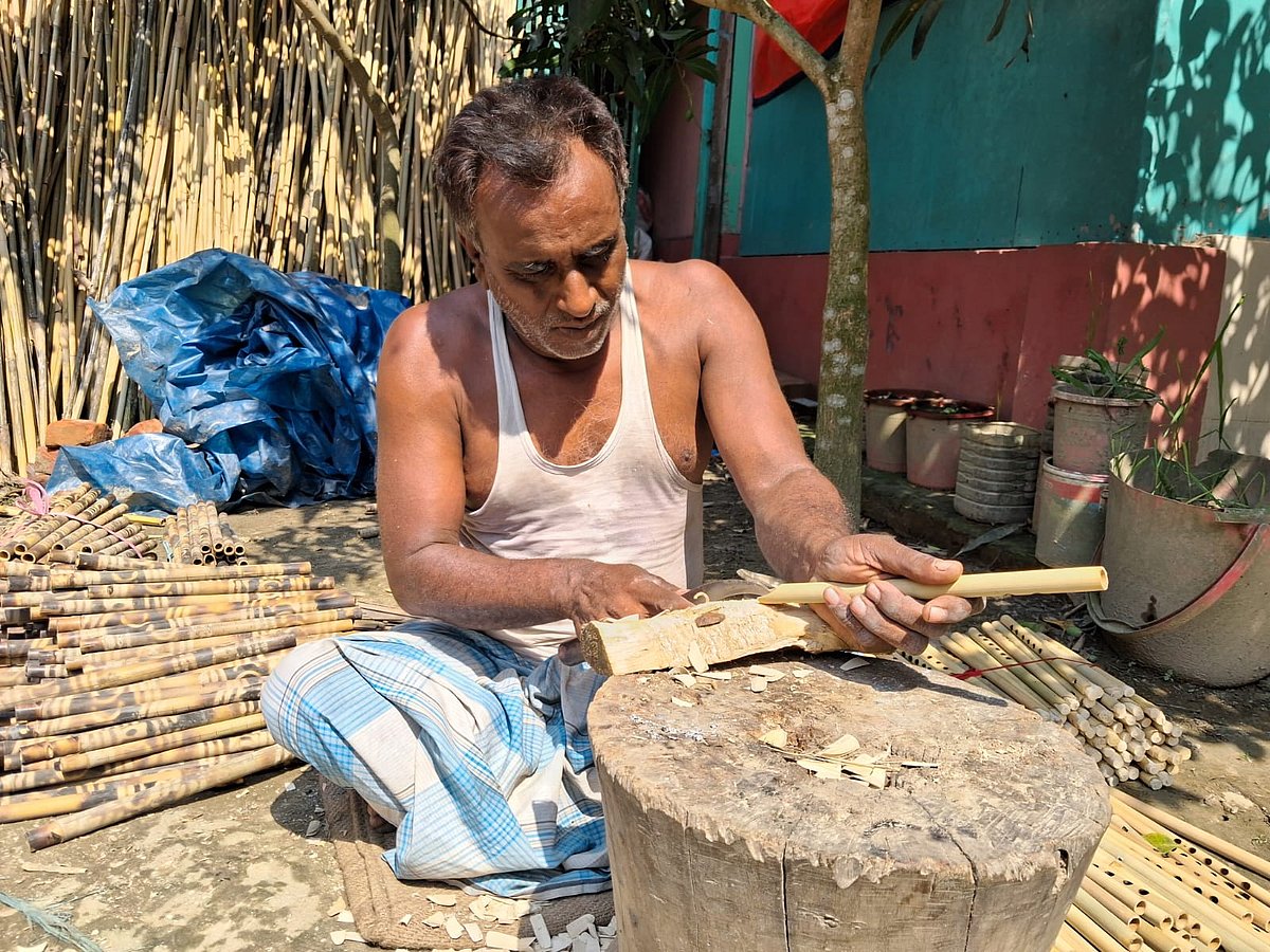 চিত্তরঞ্জন বিশ্বাস বাঁশির গায়ে ছিদ্র করার জন্য পেনসিল দিয়ে বাঁশে দাগ কাটছেন