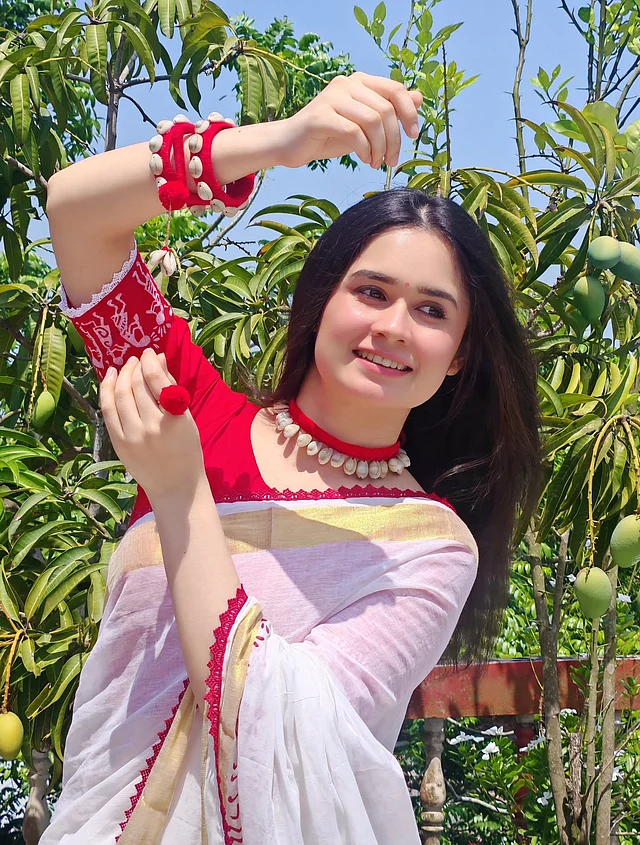 সোনালি-লাল পাড়ের সাদা শাড়ির সঙ্গে জান্নাতুল ফেরদৌস ঐশীকে দেখা যাচ্ছে লাল সুতা, পমপম আর কড়ির বোহো গয়নায়