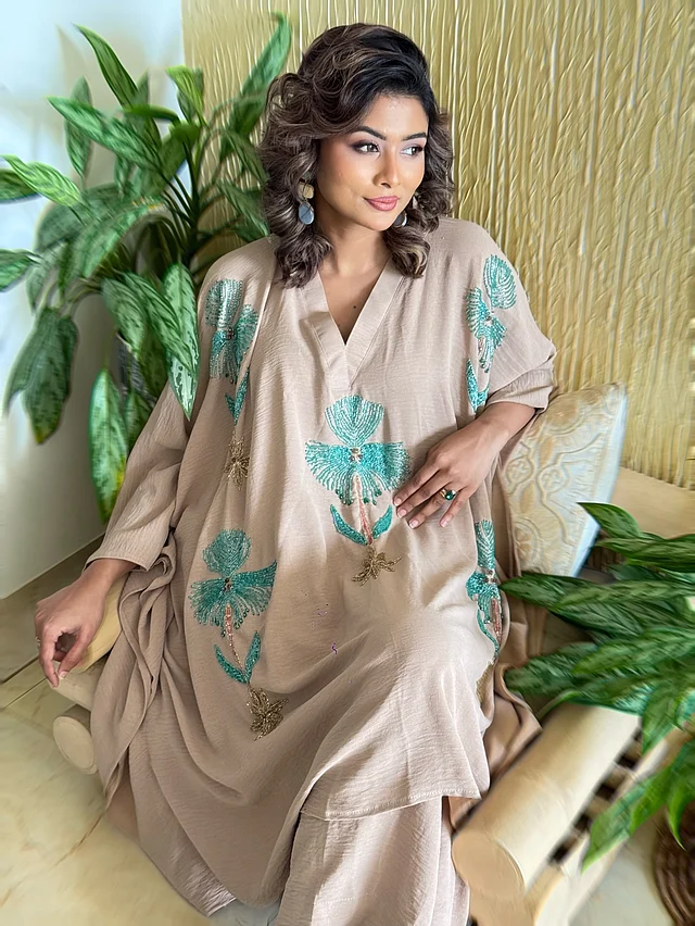 মুমতাহিনা চৌধুরী টয়া পরেছেন বেইজ রঙের একটি কাফতান সেট, যা এই আবহাওয়ার জন্য উপযুক্ত ও আরামদায়ক। টপের অংশে নীল ও সোনালি সূক্ষ্ম কারচুপি এবং বিডসের হ্যান্ড-এমব্রয়ডারি কাজ করা। 