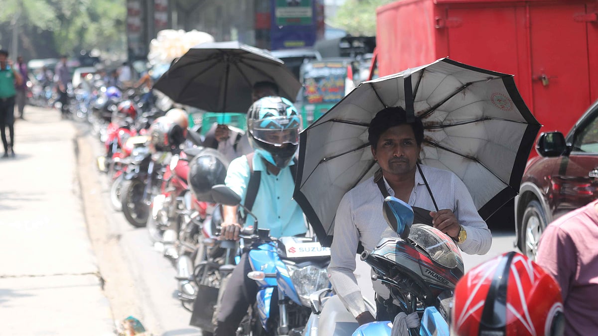 রোদ থেকে বাঁচতে ছাতা মাথায় তেল নেওয়ার জন্য অপেক্ষায় মোটরসাইকেলচালক
