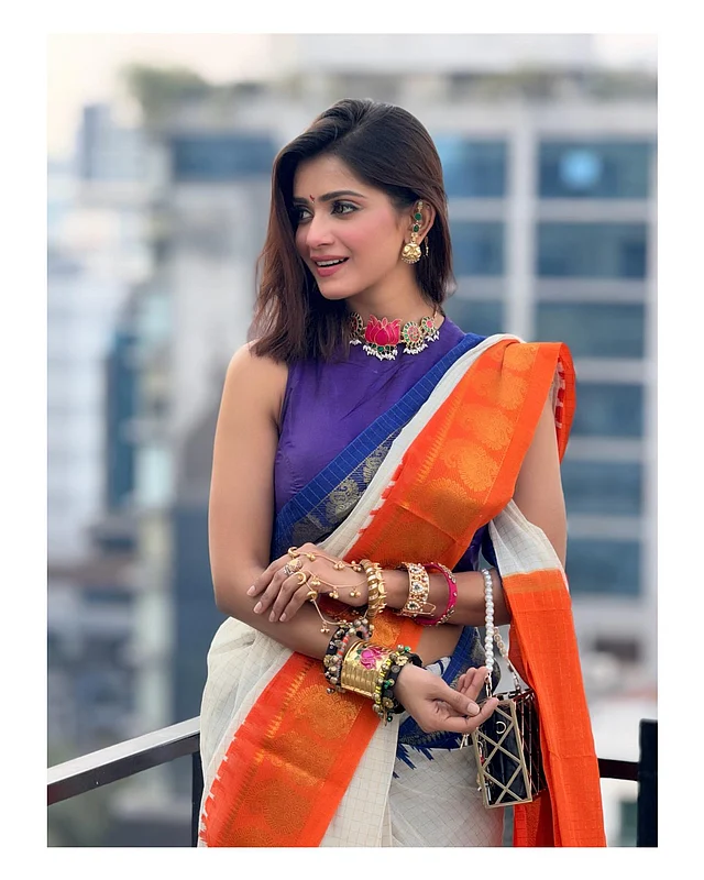 সাদা তাঁতের শাড়ি পরেছেন তিশা। তাতে উজ্জ্বল কমলা ও নেভি ব্লু গঙ্গা-যমুনা জরীপাড়