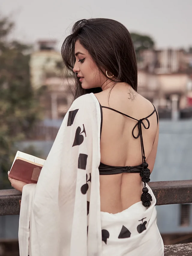 ছবিতে জেসমিনকে দেখা যাচ্ছে হাতে একটি বই নিয়ে। পরনে স্পেডস ও ডায়মন্ড মোটিফের সাদা শাড়ি, সঙ্গে ব্যাকলেস কালো ব্লাউজ। ঘাড়ের পেছনে ছোট ট্যাটু তাঁর স্টাইলকে আরও আলাদা করে তুলেছে।