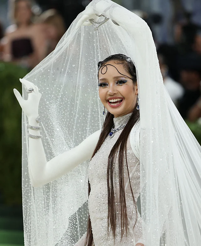 ব্ল্যাকপিংকের লিসা হাজির হন একেবারে স্বপ্নময় ও ভাস্কর্যধর্মী এক লুকে। তাঁর কাস্টম অল-হোয়াইট শিয়ার আউটফিটটি তৈরি করতে লেগেছে প্রায় ৩,০০০ ঘণ্টা।  ৬৬,৯৬০টি  ক্রিস্টাল দিয়ে সাজানো পুরো আউটফিট