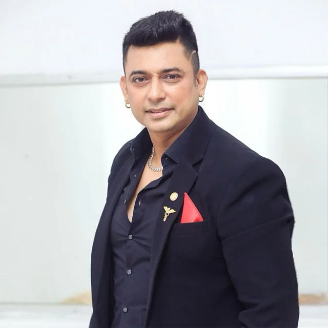 কালো স্যুটে সোনালি কোটপিন আর লাল পকেট স্কোয়্যারের সঙ্গে দুই কানের রিং দেখা যাচ্ছে 