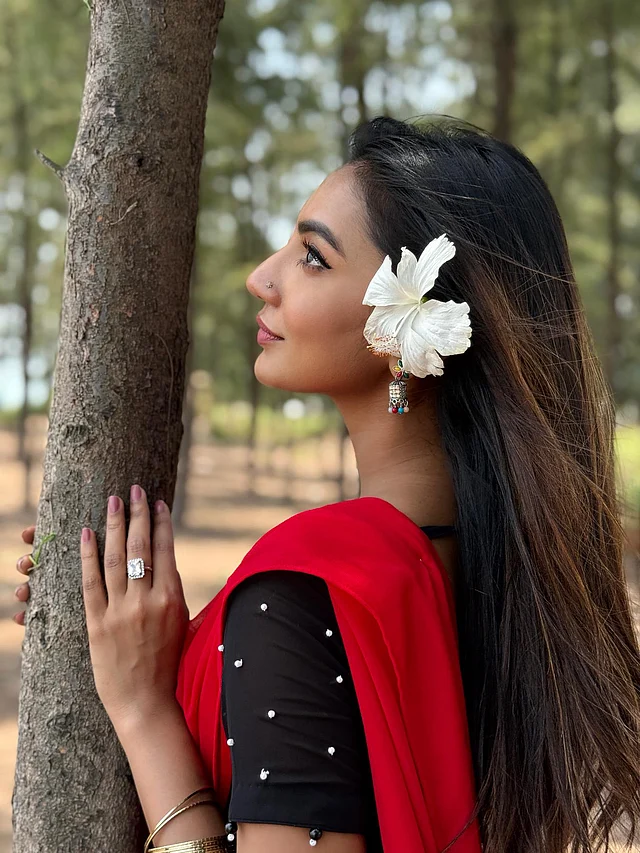 কালো ব্লাউজ আর লাল শাড়ির সঙ্গে কানের পাশে গুঁজেছেন সুনেরাহ বিনতে কামাল সাদা জবা 