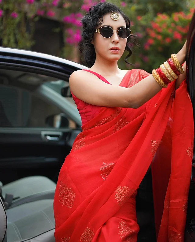 লাল শাড়ি ও স্লিভলেস ব্লাউজ আর সোনালি ওভাল ফ্রেমের কালো শেডসের সঙ্গে হাতভরা বালা আর কপালে বড় টিকলি। কে বলবে ইনি নোরা নন? 