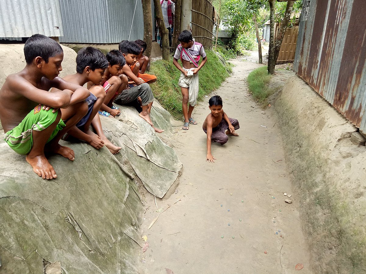 মাটিতে গর্ত করে দল বেঁধে মার্বেল খেলায় মেতে উঠেছে শিশুরা