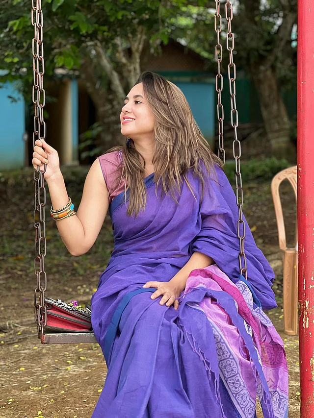 রয়েল ব্লু তাঁতের শাড়ির সঙ্গে স্লিভলেস পার্পল ব্লাউজ পরে দোলনায় বসে আছেন তিনি 