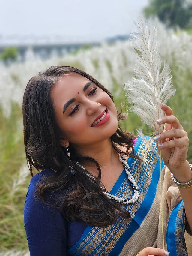 সোনালি জরীর নীল পাড়ের বেইজ কোটা শাড়ি, লাল ছট টিপ আর মানানসই গয়না পরে কাশবনে ছবি তুলেছেন তিনি 