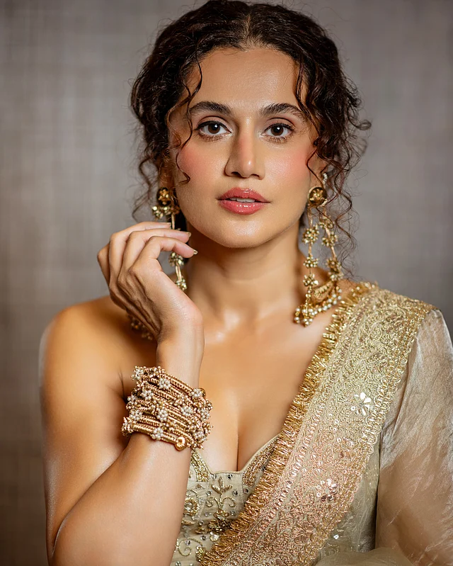 তাপসী পান্নুর এই লুকের প্রথম নজরকাড়া বিষয় তাঁর আইভরি-গোল্ড শাড়ি। ক্লাসিক উজ্জ্বলতায় মোড়া শাড়িটি তাঁকে দিয়েছে স্বপ্নিল, রাজকীয় এবং অনেকটাই অপ্সরা-সুলভ উপস্থিতি।