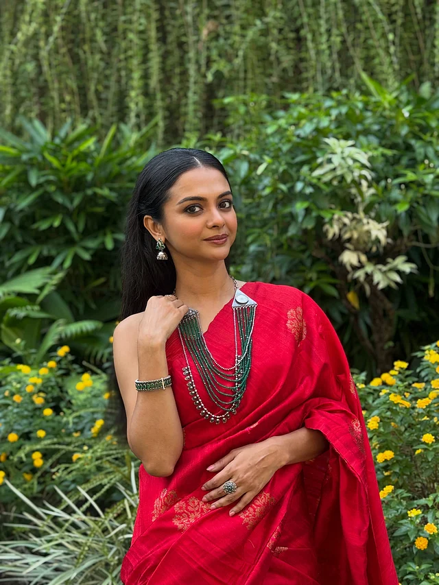 অভিনেত্রী শোলাঙ্কি রায় পরেছেন একটি  টুকটুকে লাল শাড়ি, যার জমিন জুড়ে সোনালি ব্লকের ফ্লোরাল মোটিফ রয়েছে। জুটি হয়েছে  স্লিভলেস ম্যাচিং ব্লাউজ। সাজে রয়েছে অক্সিডাইজের সঙ্গে কনট্রাস্ট সবুজ পুঁতির মাল্টি-লেয়ার হার, কানে ছোট ঝুমকা আর হাতের চুড়ি। 