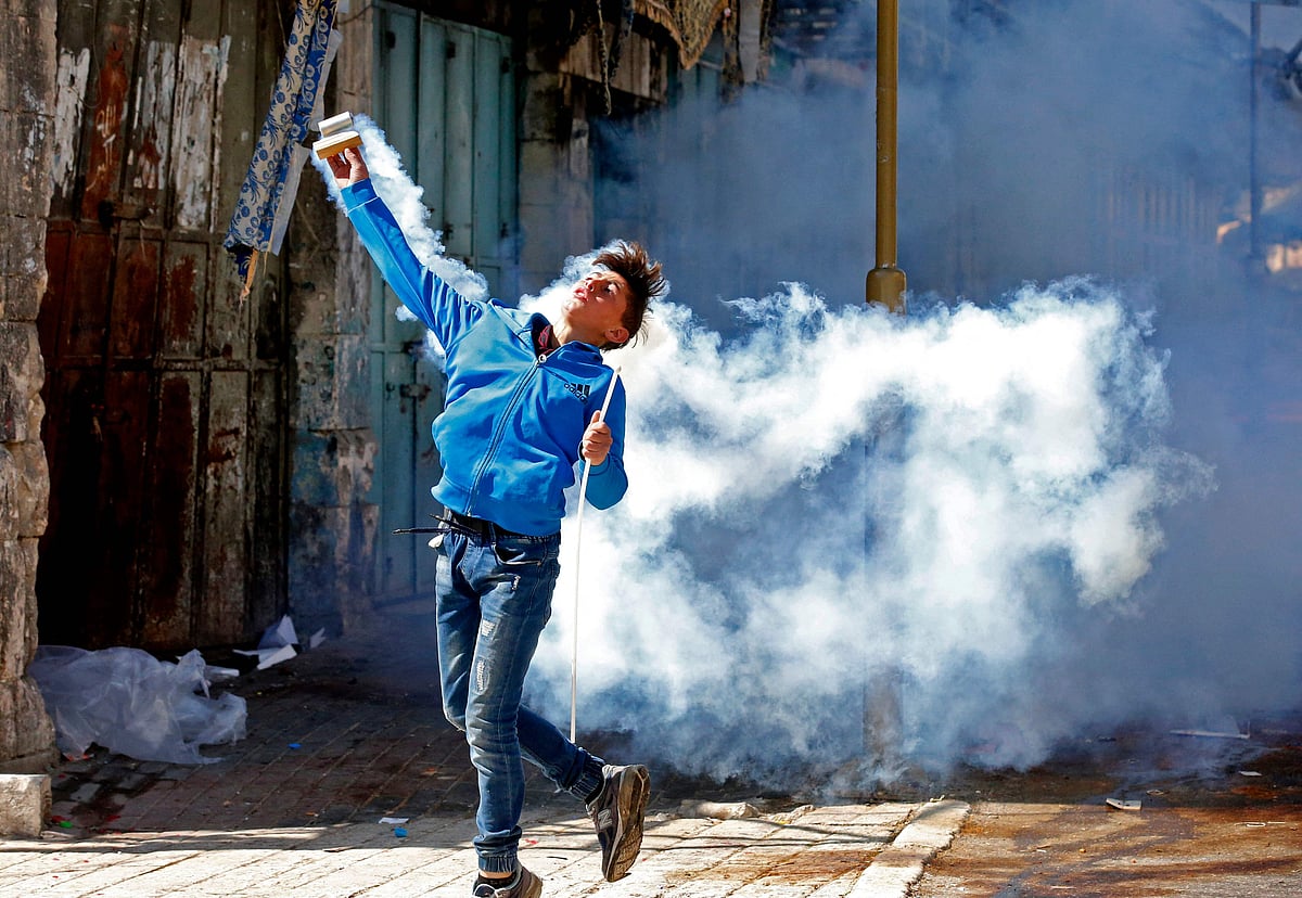 দখলকৃত পশ্চিম তীরে গতকাল শুক্রবার ইসরায়েলি সেনাদের ছোড়া কাঁদানে গ্যাসের শেল সেনাদের দিকে ছুড়ে মারছেন এক ফিলিস্তিনি তরুণ