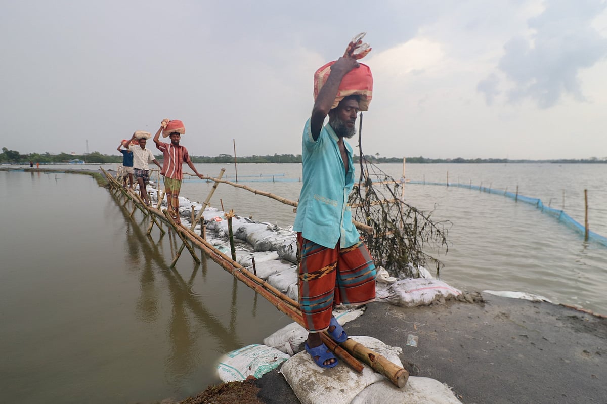জলোচ্ছ্বাসে ভেঙে যাওয়া সড়কে পাতানো সাঁকো দিয়ে খাদ্যসামগ্রী নিয়ে বাড়ি ফিরছেন দুর্ভোগে ভোগা মানুষেরা। কয়রা উপজেলার কালনা এলাকায়