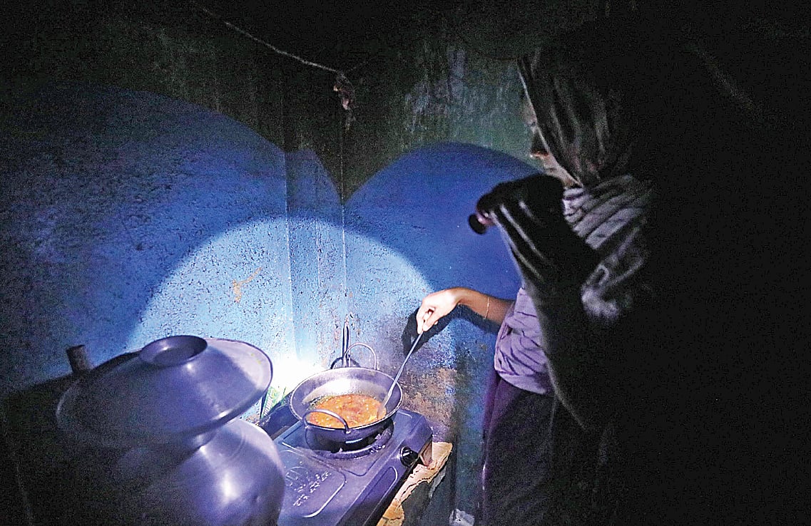 বিদ্যুৎ না থাকায় চার্জার লাইট জ্বালিয়ে রান্না করছেন এক নারী