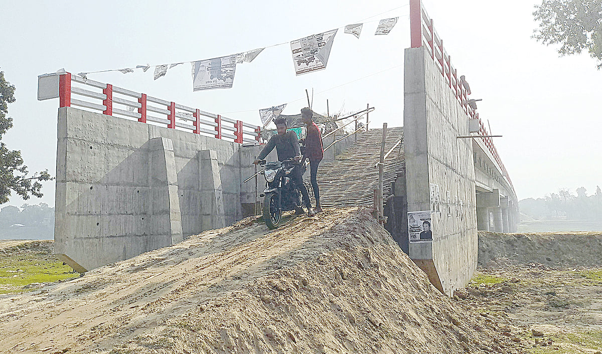 নওগাঁর মান্দা উপজেলার জোতবাজার এলাকায় নির্মিত সেতুর সংযোগ সড়ক হয়নি দেড় বছরেও। ওঠানামার জন্য বাঁশের সাঁকো করেছেন স্থানীয় লোকজনগত বুধবার।