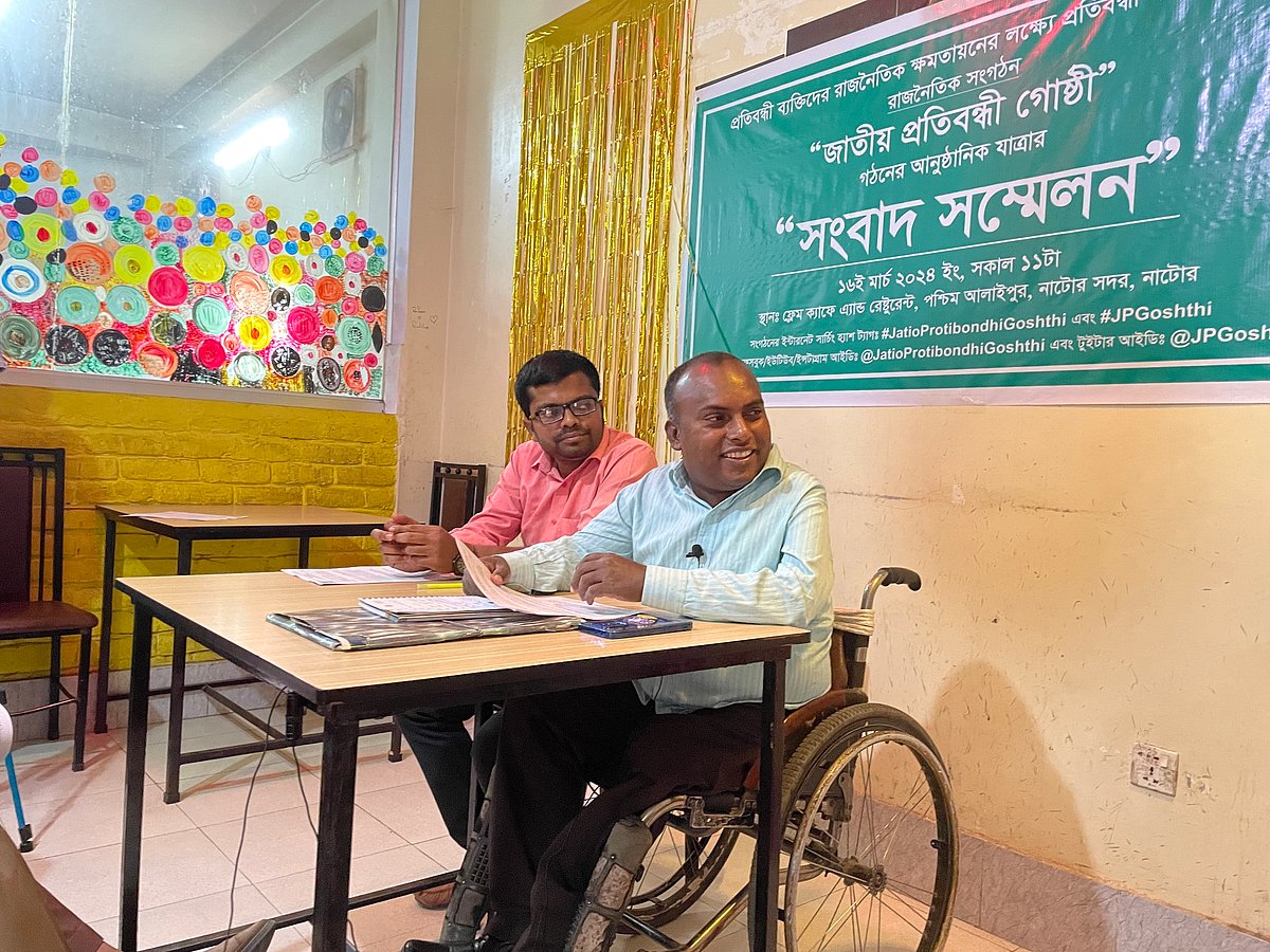 হুইলচেয়ারে বসে সংবাদ সম্মেলন করেন মহরম আলী। শনিবার দুপুরে নাটোর শহরের একটি রেস্তোরাঁয়