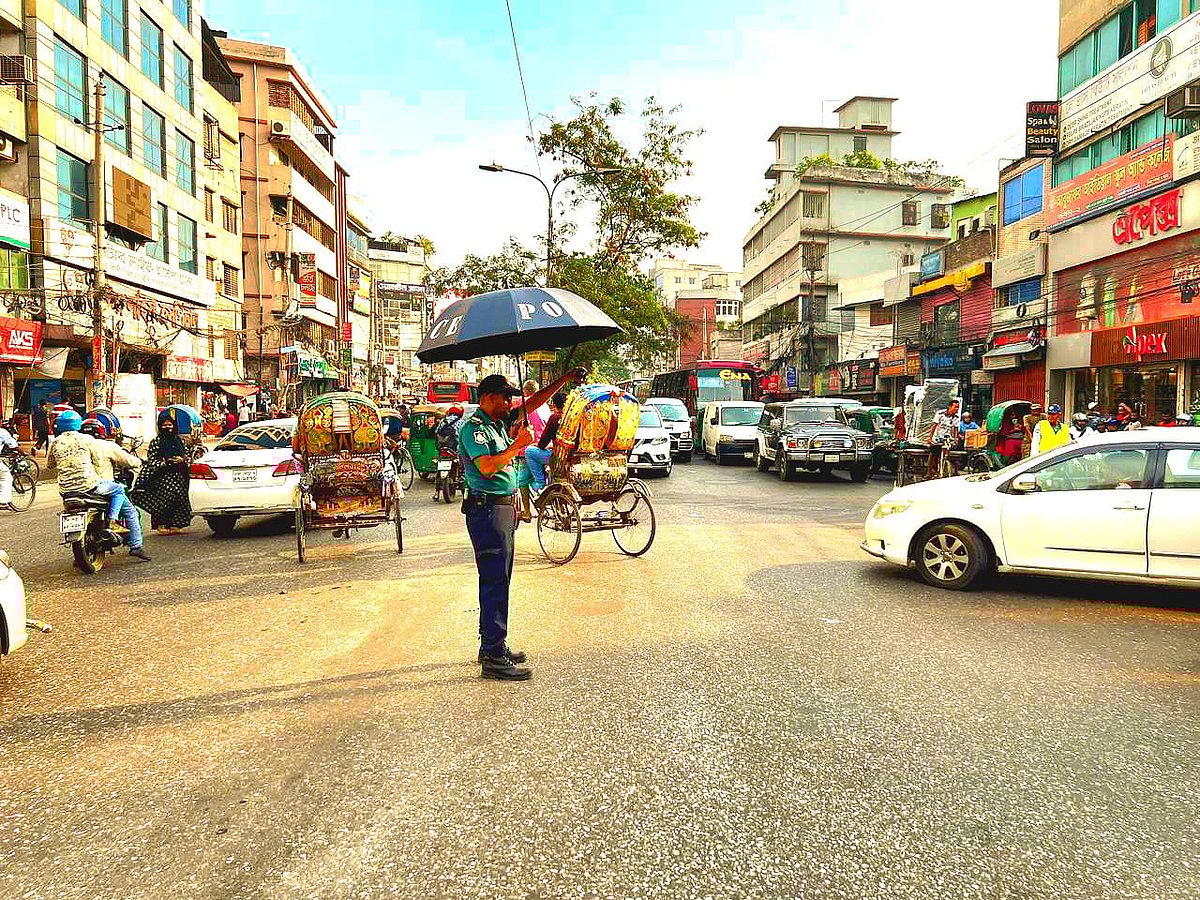 তীব্র গরমে ছাতা মাথায় সড়কে যান চলাচল নিয়ন্ত্রণ করছেন এক ট্রাফিক পুলিশ । মালিবাগ আবুল হোটের এলাকা