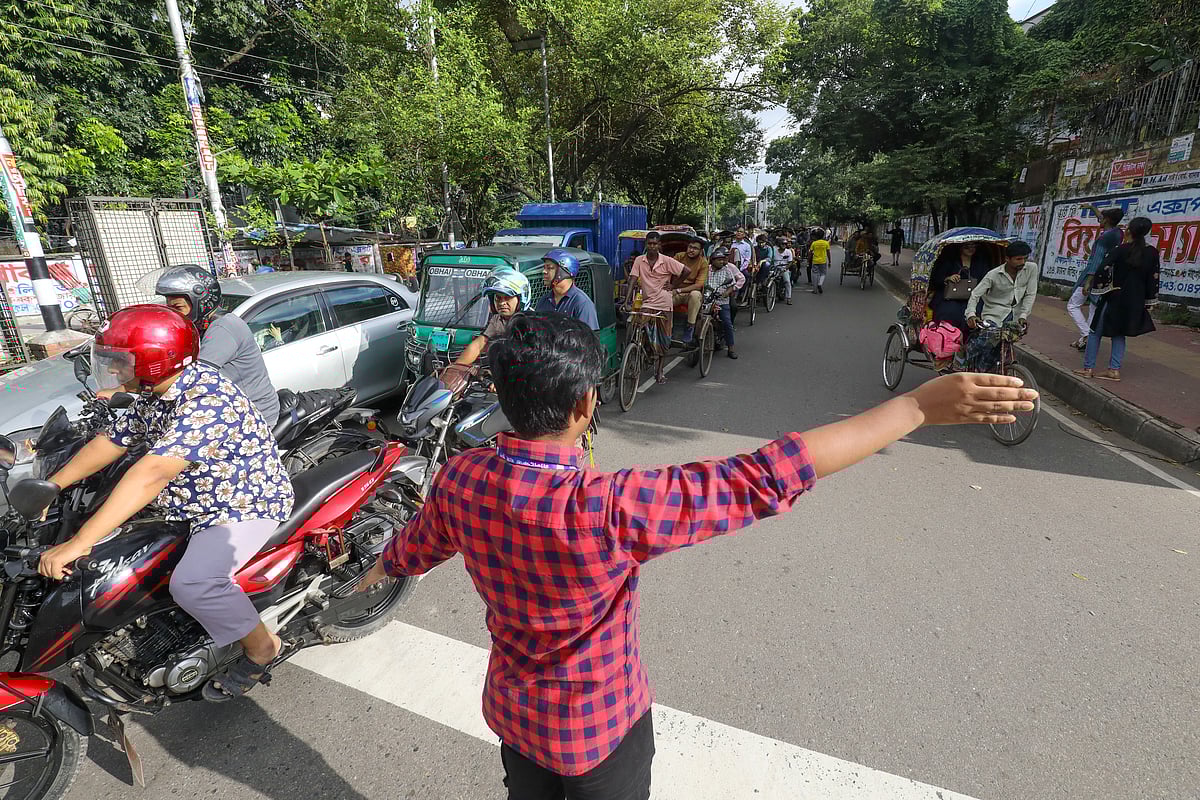হাত ইশারায় আলাদা আলাদা লেনে যানবাহন চলাচল নিয়ন্ত্রণ করছেন একজন। নীলক্ষেত, ঢাকা