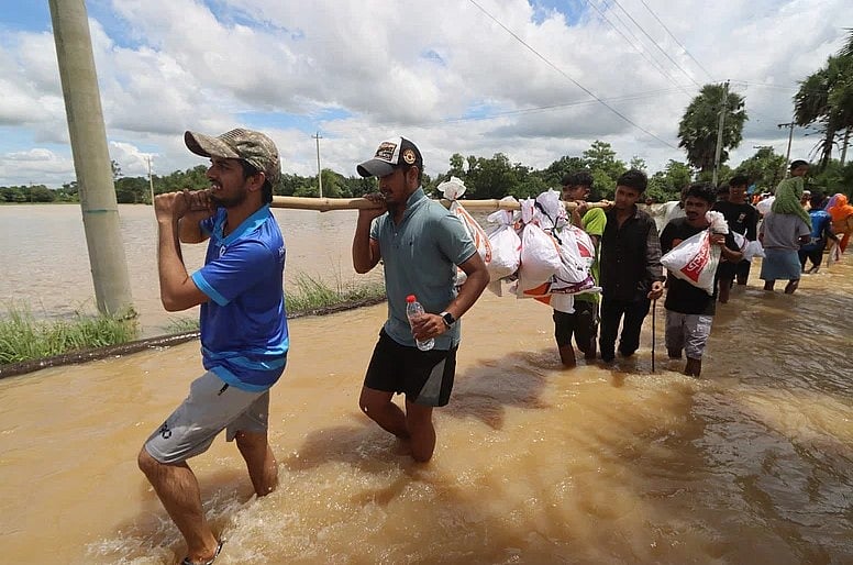 বিভিন্ন স্বেচ্ছাসেবী সংগঠনের সদস্যরা পানি মাড়িয়ে বন্যার্তদের জন্য ত্রাণসামগ্রী নিয়ে যাচ্ছেন। গাজীপুর এলাকা, বুড়িচং, কুমিল্লা, ২৪ আগস্ট
