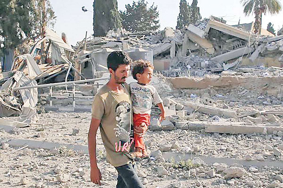 ধ্বংস হওয়া বাড়িঘরের সামনে দিয়ে সন্তান কোলে হেঁটে যাচ্ছেন এক ফিলিস্তিনি