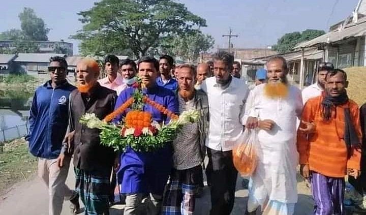 লোকজনের সঙ্গে হাতে ফুলের নৌকা নিয়ে যাচ্ছেন নুর নবী (নীল রঙের পাঞ্জাবি)