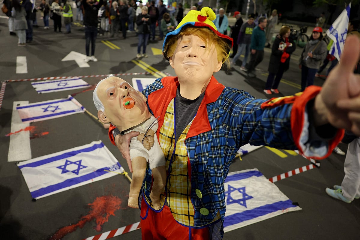 যুক্তরাষ্ট্রের নবনির্বাচিত প্রেসিডেন্ট ডোনাল্ড ট্রাম্পের মুখোশ পরে ভাঁড় সাজা এক ব্যক্তি ইসরায়েলের প্রধানমন্ত্রী বেনিয়ামিন নেতানিয়াহুর মুখোশ পরা একটি পুতুল কোলে নিয়ে জিম্মিদের মুক্তির দাবিতে বিক্ষোভ করছেন। তেল আবিবে, ১৮ জানুয়ারি ২০২৫