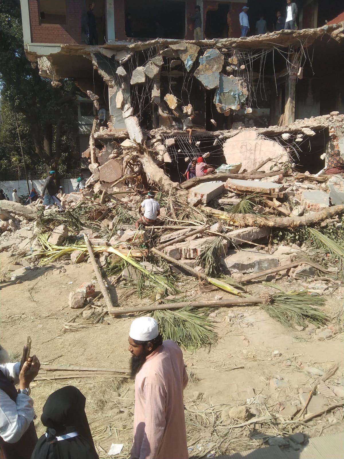 বাড়িটির ভাঙা কংক্রিটের স্ল্যাব থেকে করাত দিয়ে রড কেটে নিচ্ছেন এক ব্যক্তি। আজ শুক্রবার সকালে