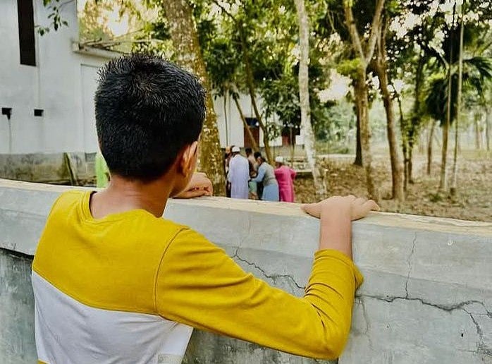 কবরস্থানের প্রাচীর ধরে পাথরের মতো দাঁড়িয়ে মায়ের কবরের দিকে তাকিয়ে আছে ১২ বছরের মেঘ। গতকাল মঙ্গলবার নাটোরের গুরুদাসপুরে