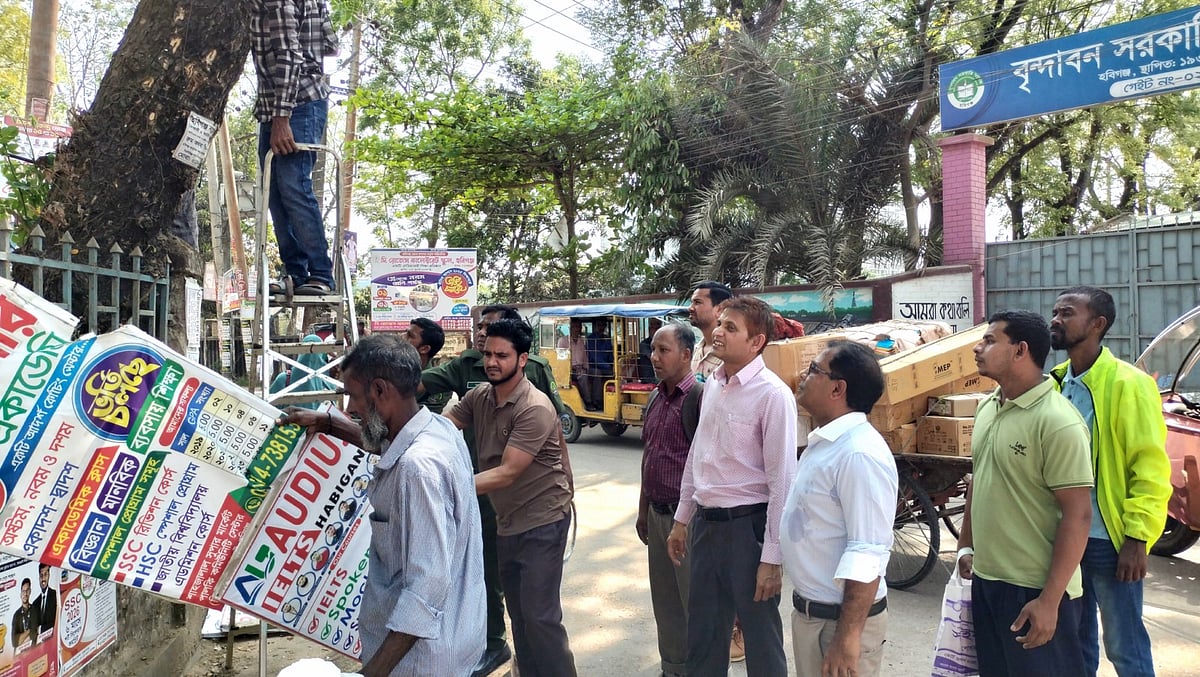 গাছের গায়ে থেকে পেরেক দিয়ে আটকানো ফেস্টুন অপসারণ করা হচ্ছে। আজ রোববার হবিগঞ্জ শহরে