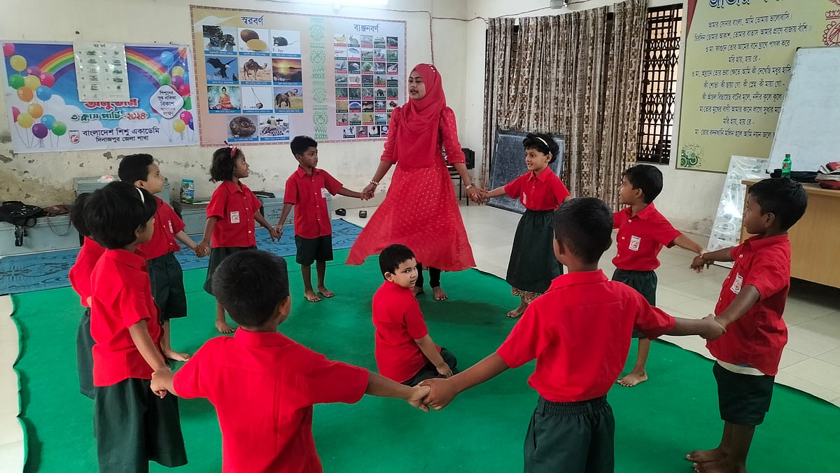 দিনাজপুর শিশু একাডেমিতে প্রশিক্ষণ ভবনের নিচতলায় প্রাক-প্রাথমিকের শিক্ষার্থীদের ছড়া শোনাচ্ছেন শিক্ষক