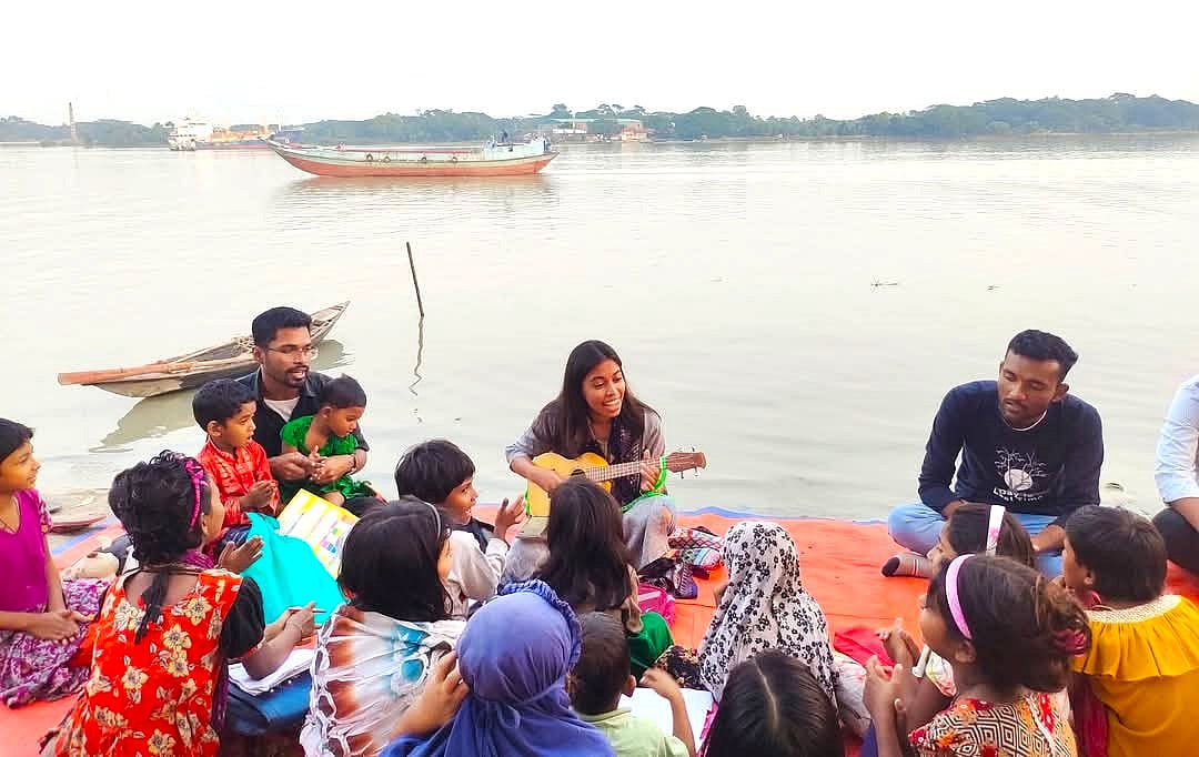 কীর্তনখোলা নদীর পারে পাঠদান শেষে গিটার নিয়ে বিশ্ববিদ্যালয়শিক্ষার্থীদের সঙ্গে কোরাস গাইছে শিশুরা। শনিবার বিকেলে বরিশাল নগরের কীর্তনখোলা নদীতীরের চাঁনমারি এলাকায়