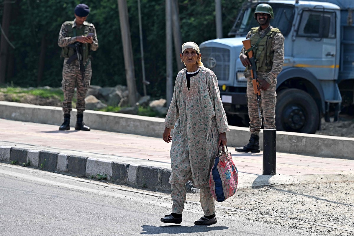 দাঁড়িয়ে আছেন দুই সেনা, তাঁদের সামনে দিয়ে হেঁটে যাচ্ছেন এক নারী। ভারতনিয়ন্ত্রিত কাশ্মীরের শ্রীনগরে, ১ মে ২০২৫