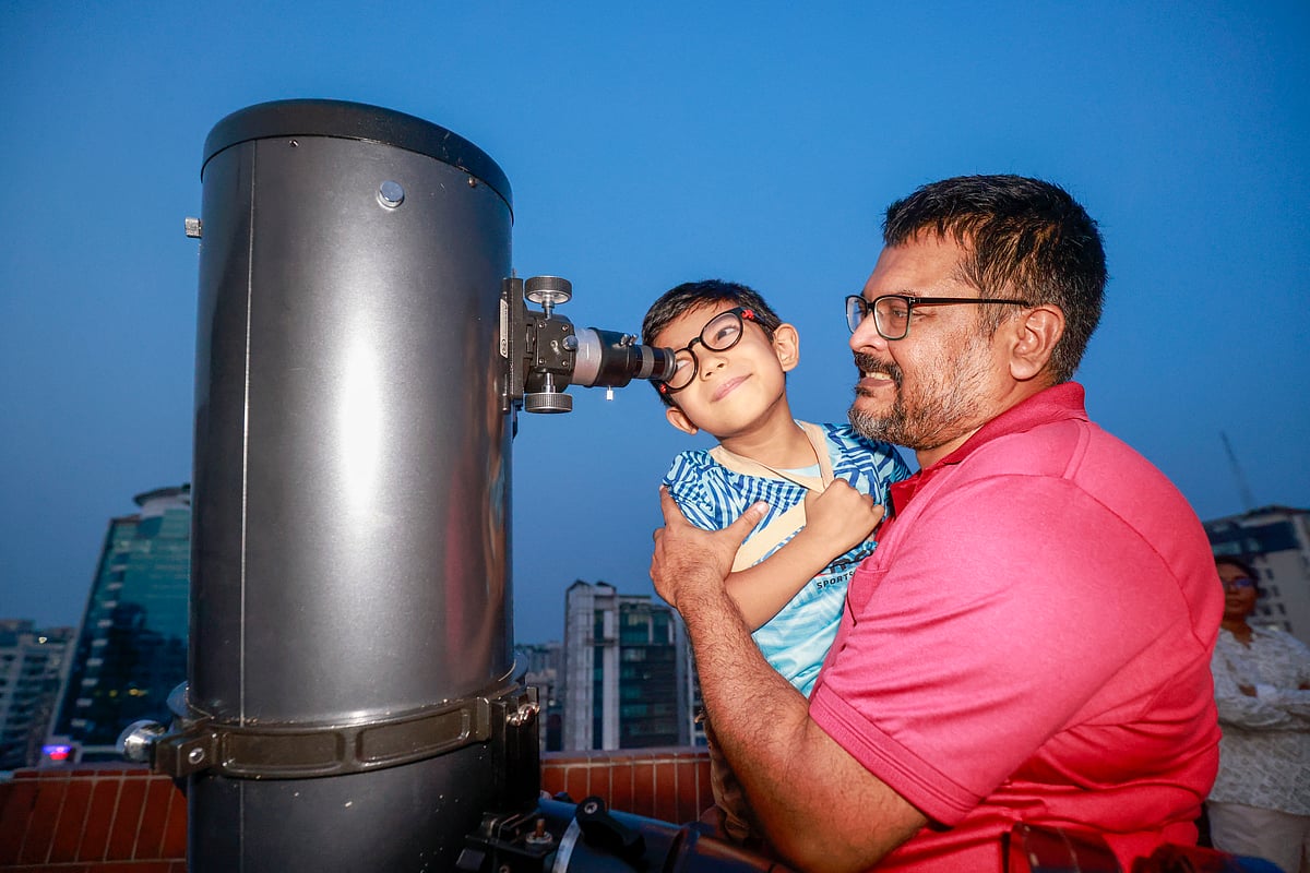 এক ব্যক্তির কোলে চড়ে দুরবিনে চোখ রেখে আকাশ পর্যবেক্ষণ করছে এক শিশু। এই আকাশ পর্যবেক্ষণ ক্যাম্পের আয়োজন করে বাংলাদেশ অ্যাস্ট্রোনমিক্যাল অ্যাসোসিয়েশন। রাজধানীর বাংলামোটরে অবস্থিত বিশ্বসাহিত্য কেন্দ্রে, ৩ মে ২০২৫