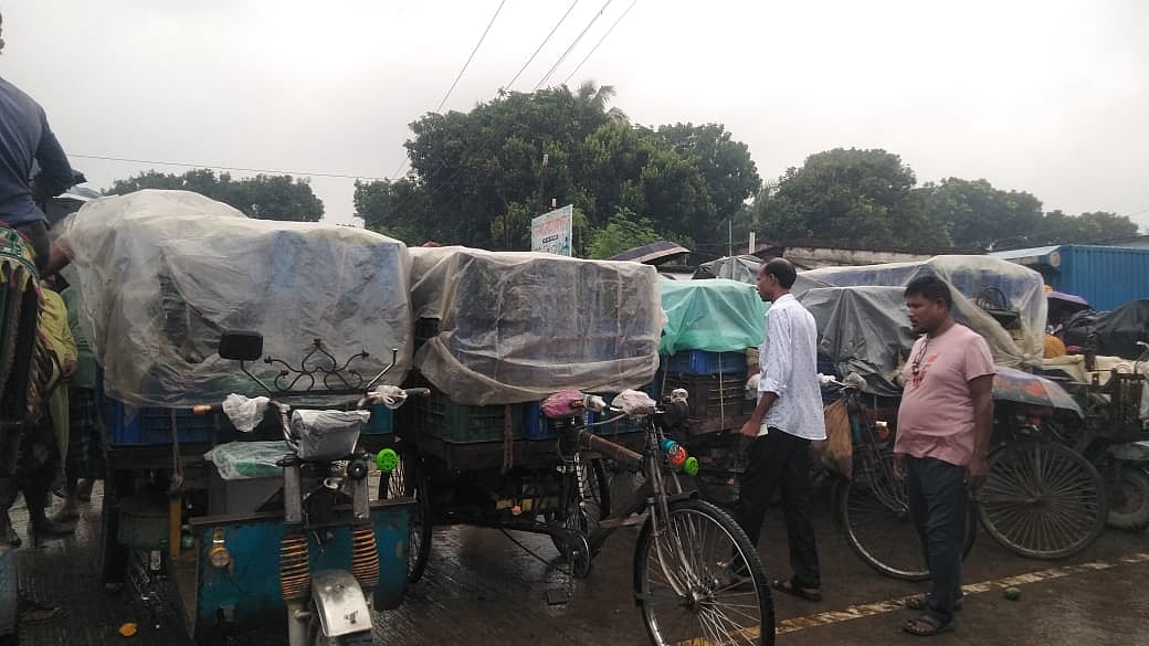 বৃষ্টির মধ্যে ভ্যানে আম নিয়ে দাঁড়িয়ে আছেন ব্যবসায়ীরা। আজ বৃহস্পতিবার দুপুরে রাজশাহীর পুঠিয়ার বানেশ্বর বাজারে