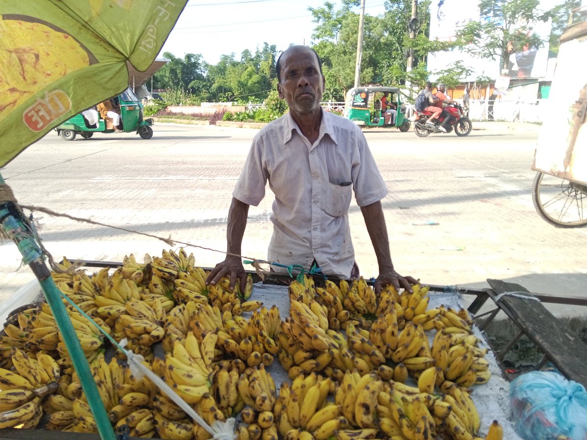 শাহজালাল বিজ্ঞান ও প্রযুক্তি বিশ্ববিদ্যালয়ের প্রধান ফটকের পাশে নিজের ঠেলাগাড়িতে কলা সাজিয়ে বিক্রি করছেন হরিচরণ দাস। সম্প্রতি তোলা