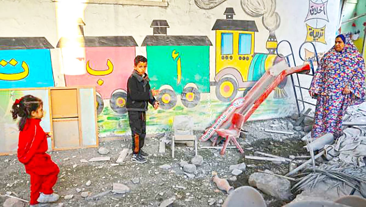 গাজায় ইসরায়েলি বোমা হামলায় বিধ্বস্ত বিদ্যালয়ের সামনে দঁাড়িয়ে আছে ফিলিস্তিনি দুটি শিশু ও এক নারী