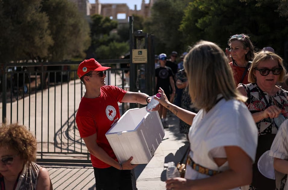 হেলেনিক রেডক্রসের এক স্বেচ্ছাসেবক গ্রিসের এথেন্সে অ্যাক্রোপলিস পরিদর্শনকারীদের মধ্যে পানির বোতল বিতরণ করছেন। ৯ জুলাই ২০২৫