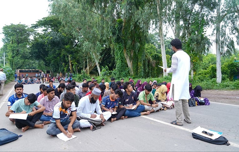 সিরাজগঞ্জের শাহজাদপুরে রবীন্দ্র বিশ্ববিদ্যালয়ের স্থায়ী ক্যাম্পাস নির্মাণ প্রকল্পের ডিপিপি (উন্নয়ন প্রকল্প প্রস্তাব) অনুমোদনের দাবিতে মহাসড়কে প্রতীকী ক্লাস শিক্ষার্থীদের। মঙ্গলবার সকাল ১০টার দিকে শাহজাদপুরে রবীন্দ্র বিশ্ববিদ্যালয়ের অস্থায়ী একাডেমিক ভবন-৩ এর সামনে নগরবাড়ী-বগুড়া মহাসড়কে