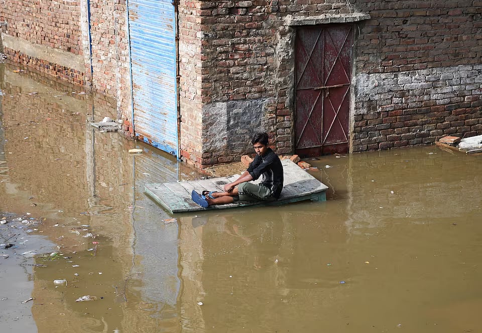 বন্যার পানিতে ডুবে যাওয়া সড়কে একটি কাঠের টেবিলের ওপর বসে আছেন এক ব্যক্তি। পাকিস্তানের হায়দরাবাদের লতিফাবাদ এলাকা থেকে সম্প্রতি তোলা