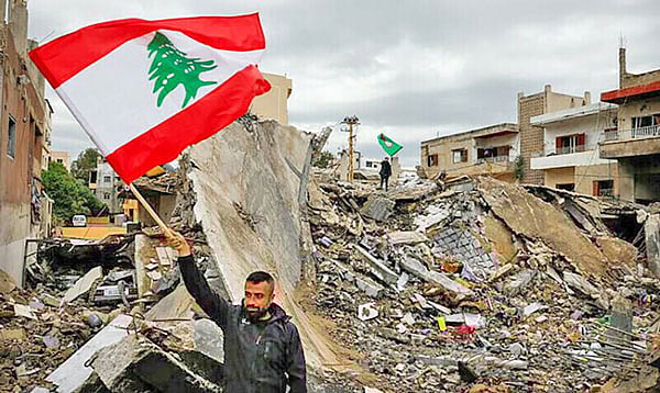 ইসরায়েলের হামলায় বিধ্বস্ত স্থাপনার সামনে পতাকা হাতে এক লেবাননি