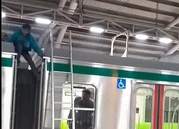 মেট্রোরেলের ছাদে উঠে পড়া একজন নেমে আসছেন। আজ রোববার রাতে ঢাকার সচিবালয় স্টেশনে