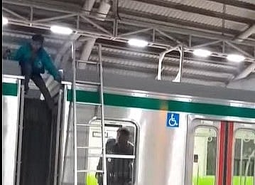 মেট্রোরেলের ছাদে উঠে পড়া একজন নেমে আছেন। আজ রোববার রাতে ঢাকার সচিবালয় স্টেশনে