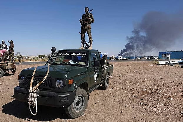 গাড়ির ওপর দাঁড়িয়ে আছেন সুদানের সেনাবাহিনীর সদস্য। পেছনে জ্বলছে তেল পরিশোধনাগার। সুদানের উত্তর বাহরি প্রদেশ, জানুয়ারি ২০২৫