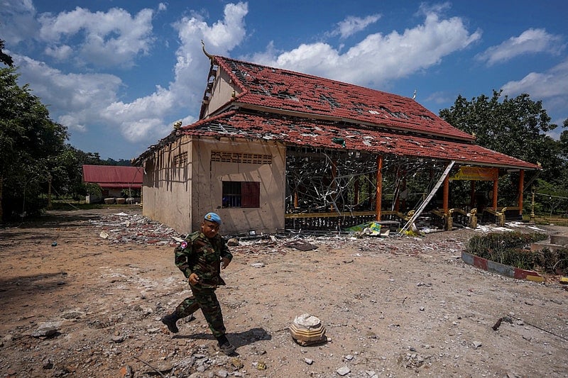 কম্বোডিয়ায় গোলার হামলায় বিধ্বস্ত একটি ভবনের সামনে দিয়ে হেঁটে যাচ্ছেন দেশটির এক সেনা