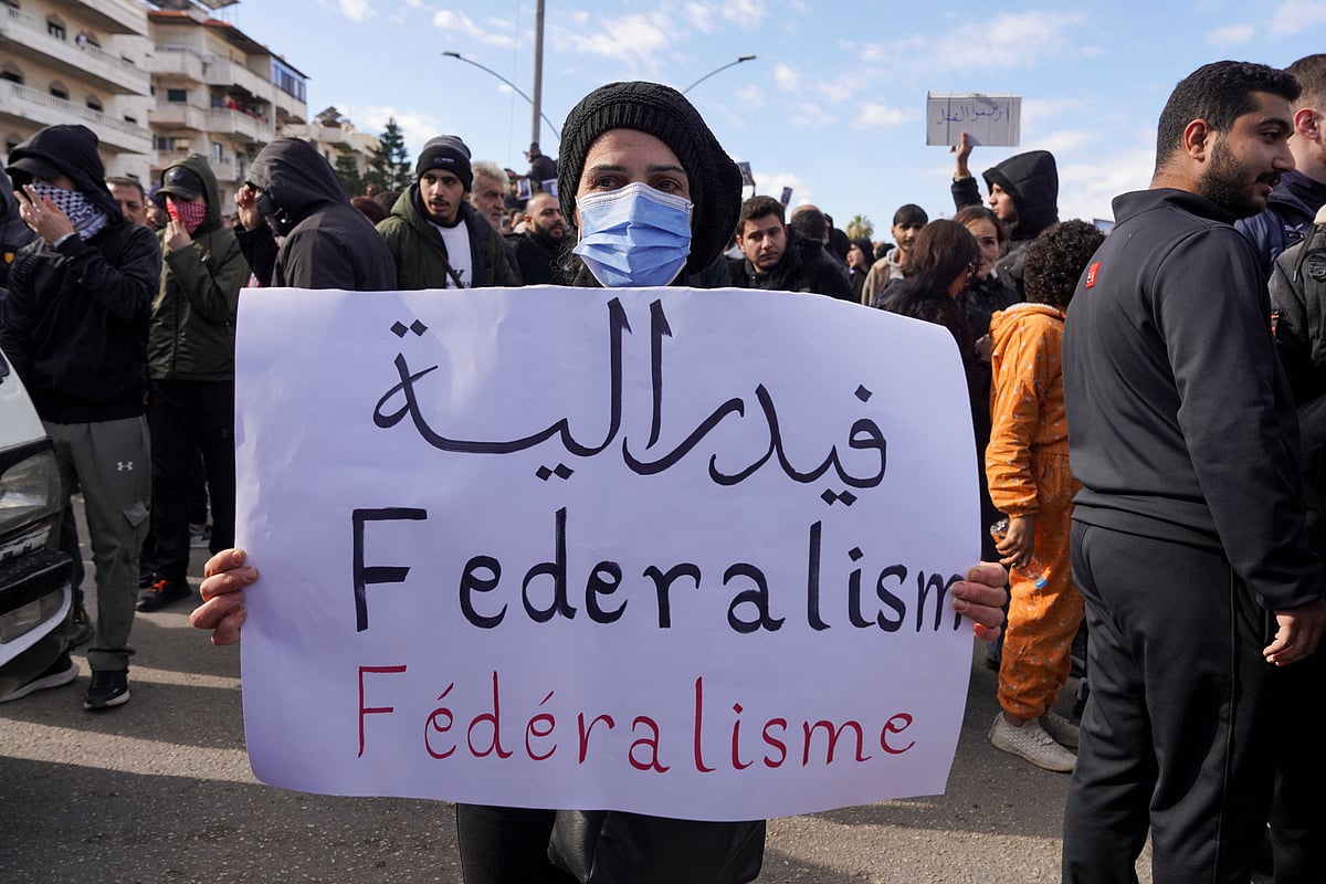 ফেডারেল সরকারব্যবস্থার দাবি–সংবলিত একটি প্ল্যাকার্ড হাতে আলাউইত জনগোষ্ঠীর এক ব্যক্তি। সিরিয়ার লাতাকিয়ায়, ২৮ ডিসেম্বর ২০২৫