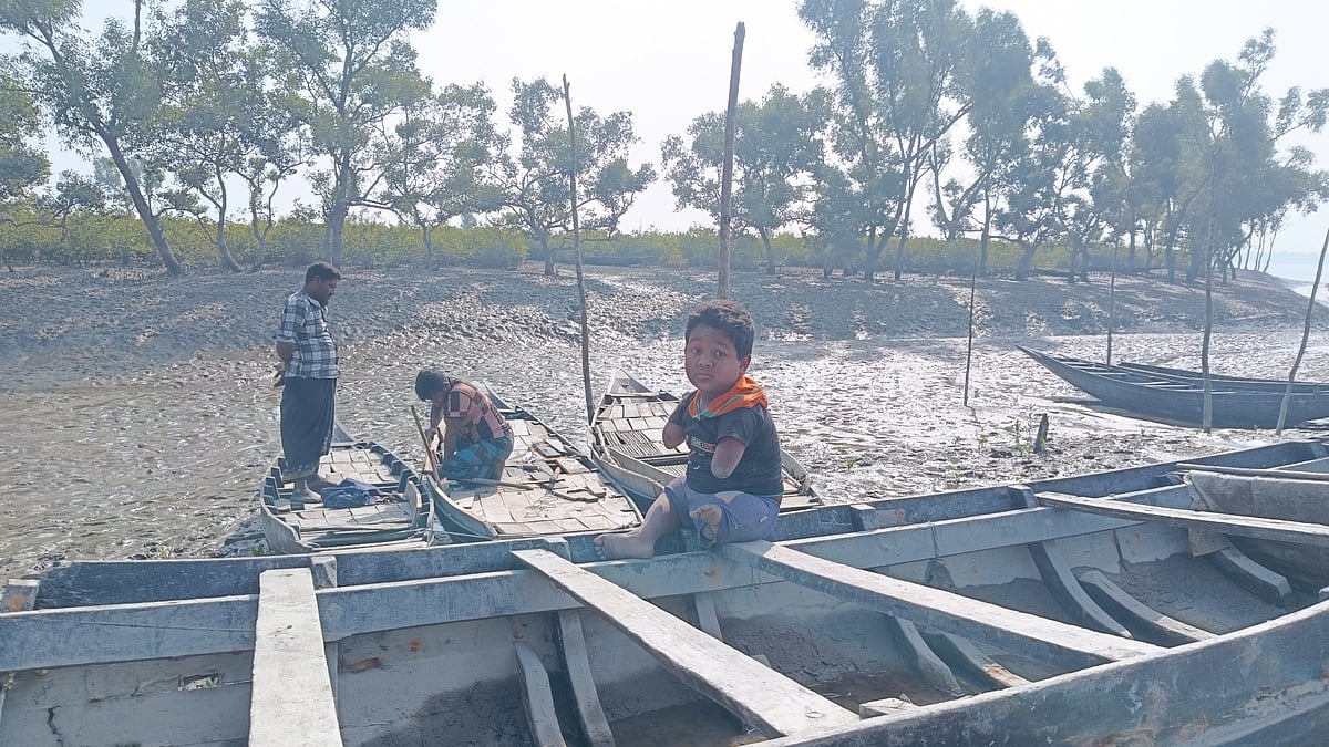 আড়পাঙ্গাসিয়া নদীর তীরে বাবা আলাউল ইসলাম নৌকার পাটাতন ঠিক করছেন। পাশের আরেকটি নৌকায় বসে আছে শিশু সিয়াম। ১ জানুয়ারি খুলনার কয়রা উপজেলার গোলখালী গ্রামে